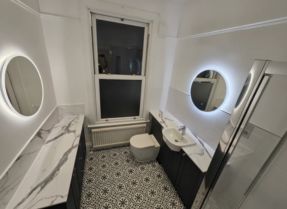 Luxury bathroom renovation with marble worktops, patterned floor tiles and round LED mirrors, North London